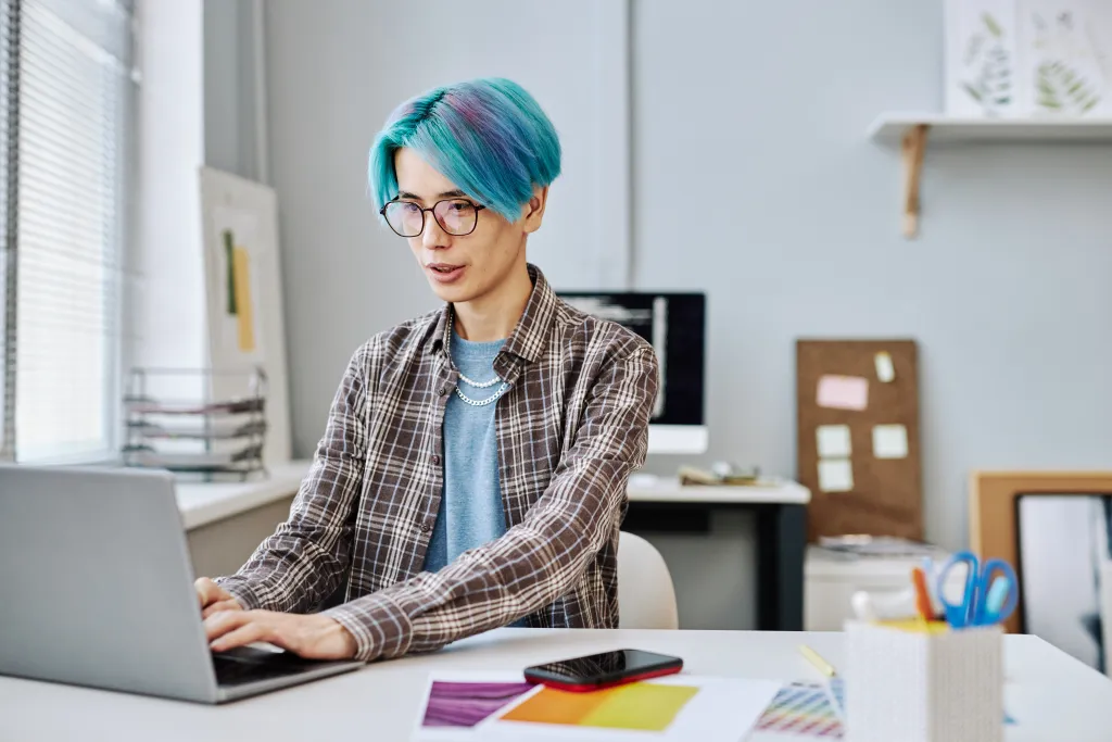 creative-young-man-with-blue-hair-using-laptop-in-office.webp